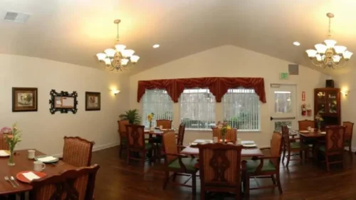 A panoramic view of a dining room with multiple tables set for meals, chandeliers, and framed art on the walls